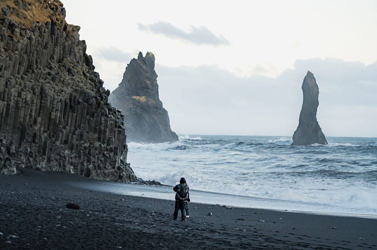 Tourists taking photos on Reynisfjara black sand beach with basalt columns and ocean waves in the background.