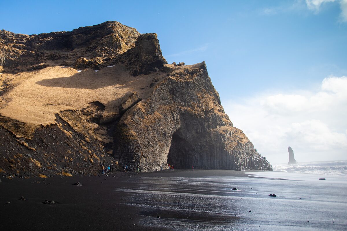 Basalt columns cliff rock at Reynisfjara beach on sunny day with bright blue skies.
