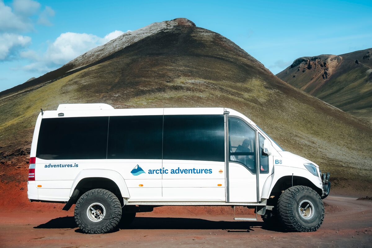 White Arctic Adventures tour bus parked in front of mountain at Landmannalaugar, in the Icelandic highlands.
