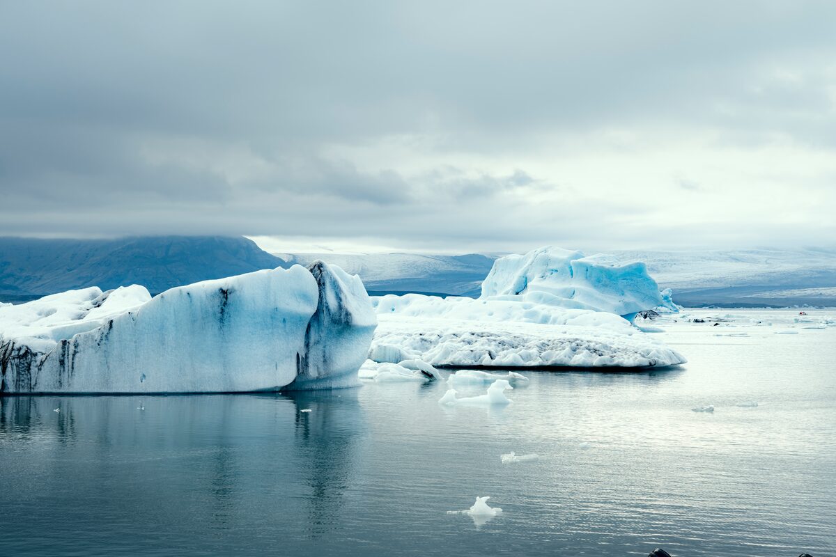 Large white blue and black patterned icebergs floating on Jokulsarlon glacier lagoon in summer, grey skies.