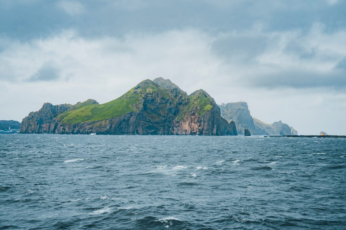 Vestmannaeyjar island rocky cliffs and lushious green growth from sea view.