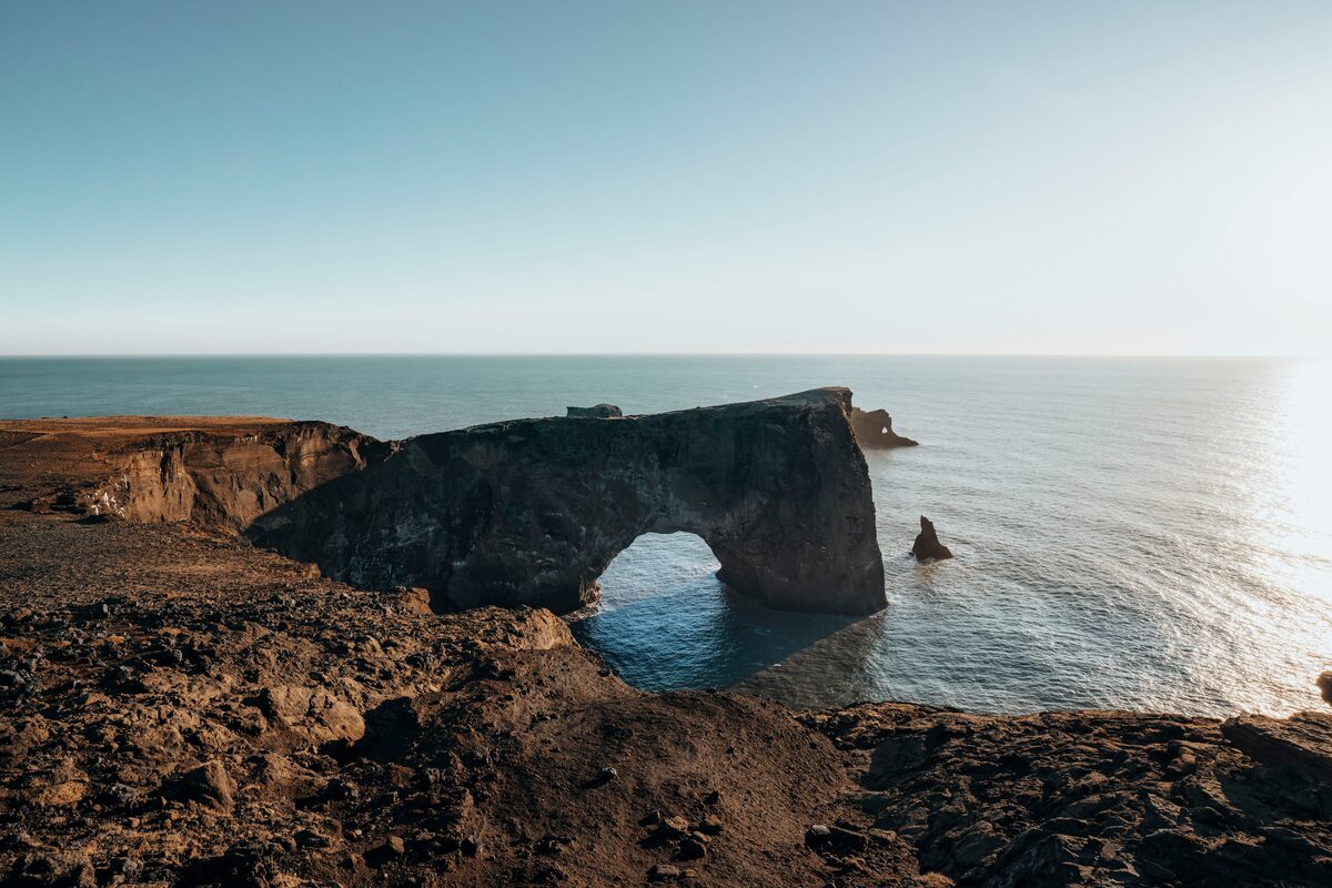 The Dyrhólaey sea arch in Iceland silhouetted against a vibrant sunset sky, with golden light reflecting off the ocean below.