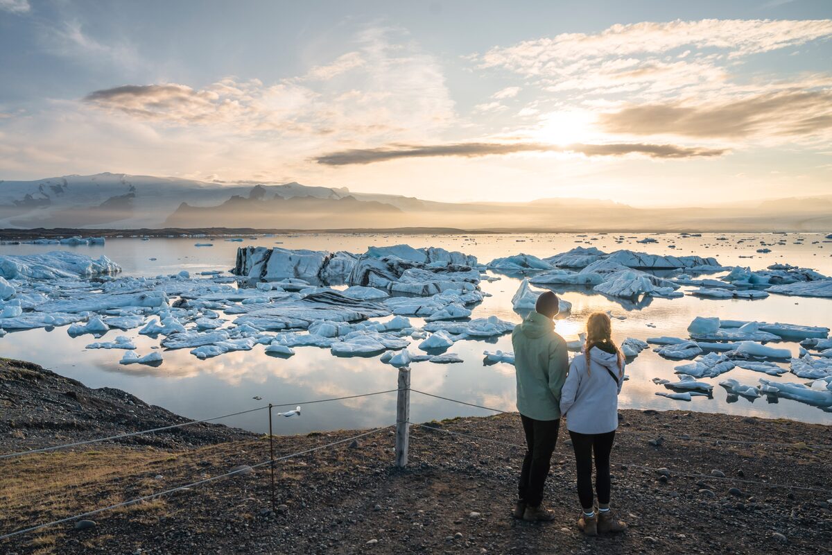 A young couple stands together, admiring the glowing summer sunset over Jökulsárlón glacier lagoon in Iceland.