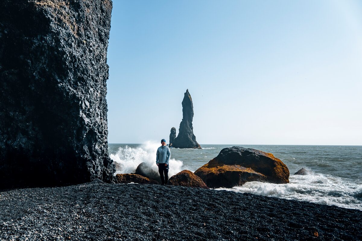 Female posing by the crashing waves at Reynisfjara black sand beach in summer.