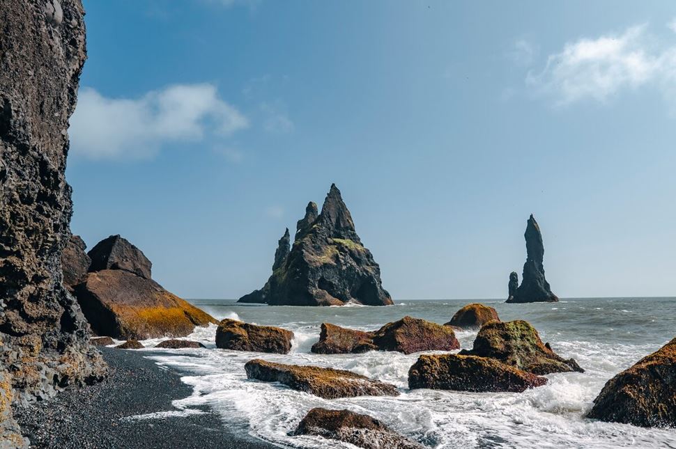 Rocks, cliffs, and basalt columns rising from the sea at Reynisfjara Beach, Iceland during summer.