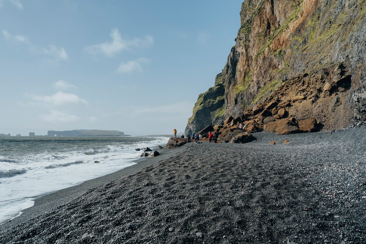 The black sand shoreline of Reynisfjara Beach in Iceland, stretching along the coast with waves lapping at the shore.