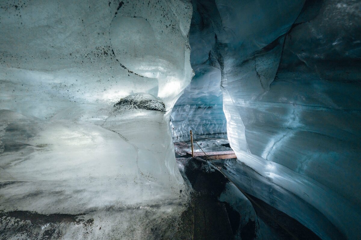 Inside Katla Ice Cave, showing a wooden plank footpath over the icy floor, surrounded by textured blue and white ice walls with natural patterns.