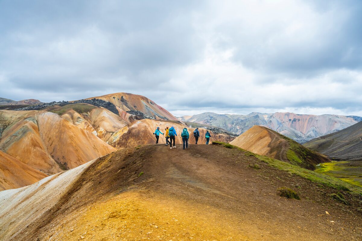 Group in the distance hiking across Laugavegur trail in the highlands of Iceland, colorful mountains in background.