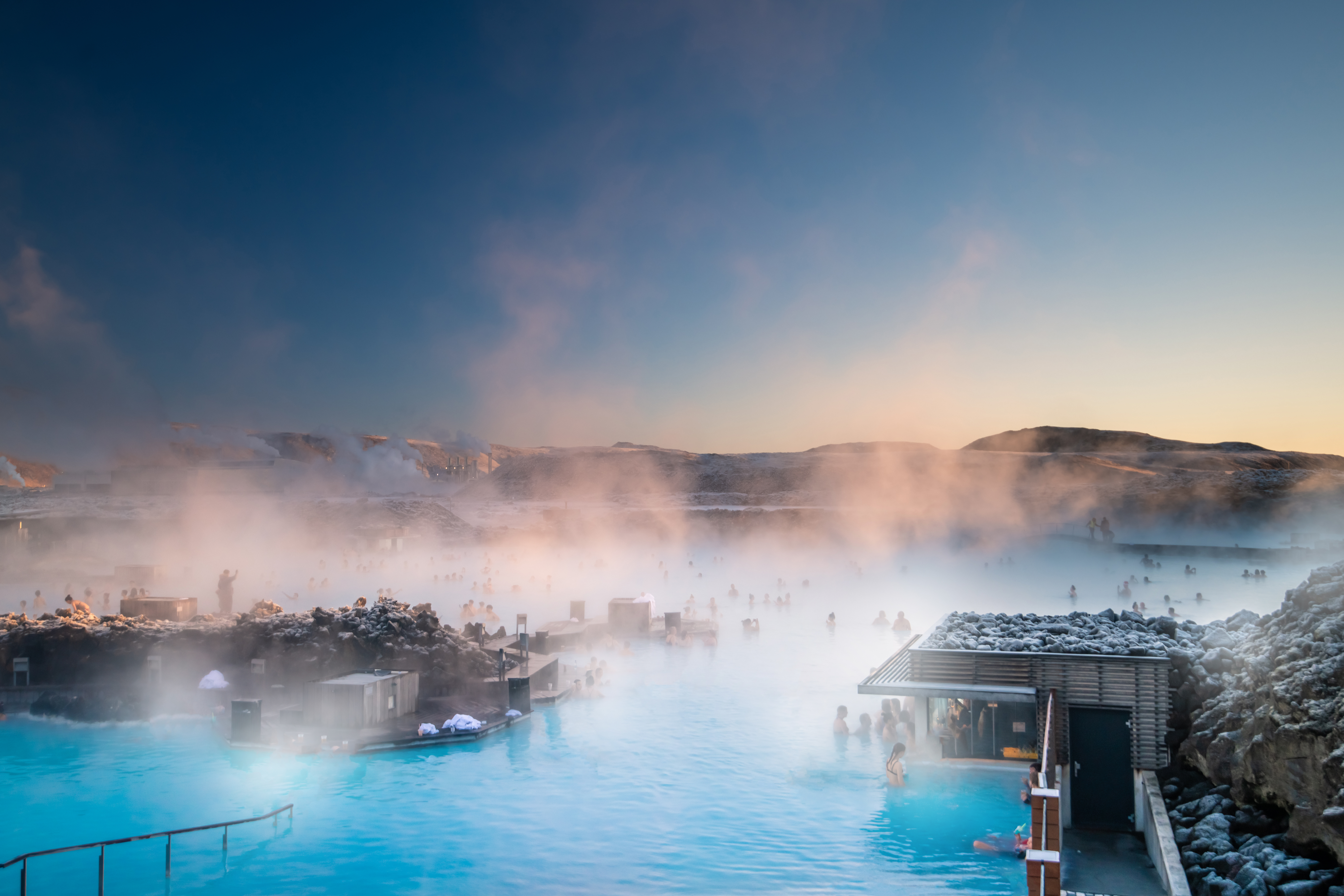 Landscape shot of the blue lagoon in Iceland during winter, steam rising from the hot blue waters and snow settling on rocks surrounding the lagoon.