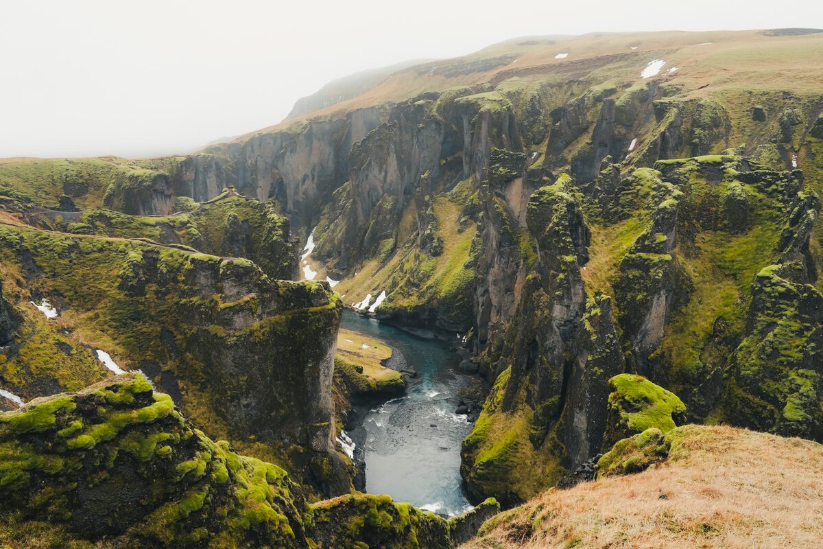 Fjardargljufur canyon covered in thick moss with scattered snow fall, a turquoise stream running in between canyon in Iceland.