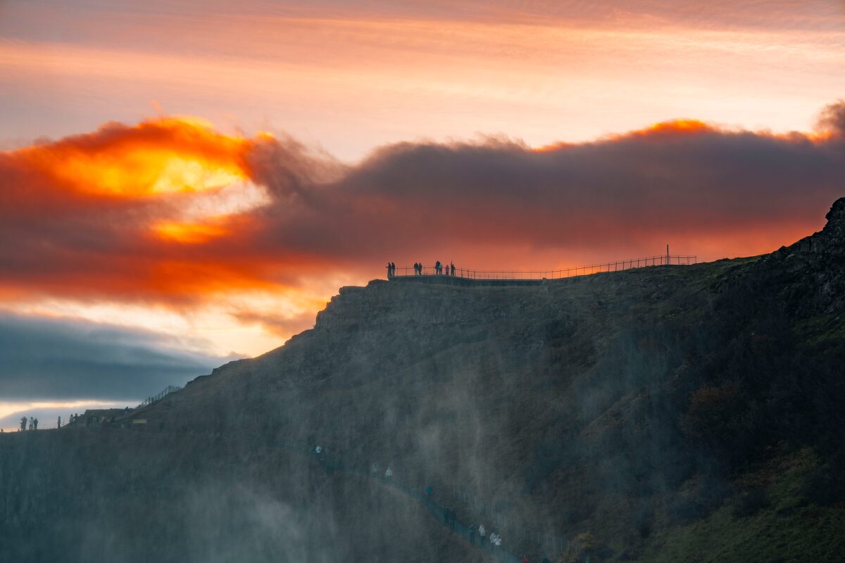 Silouhettes of small group of people standing on Gullfoss waterfall cliffs during a sunset in autumn.