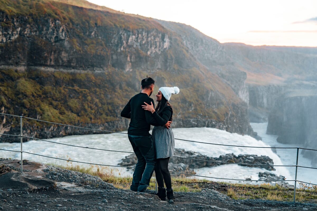 Couple standing behind safety fence, viewing Gullfoss waterfall in autumn.