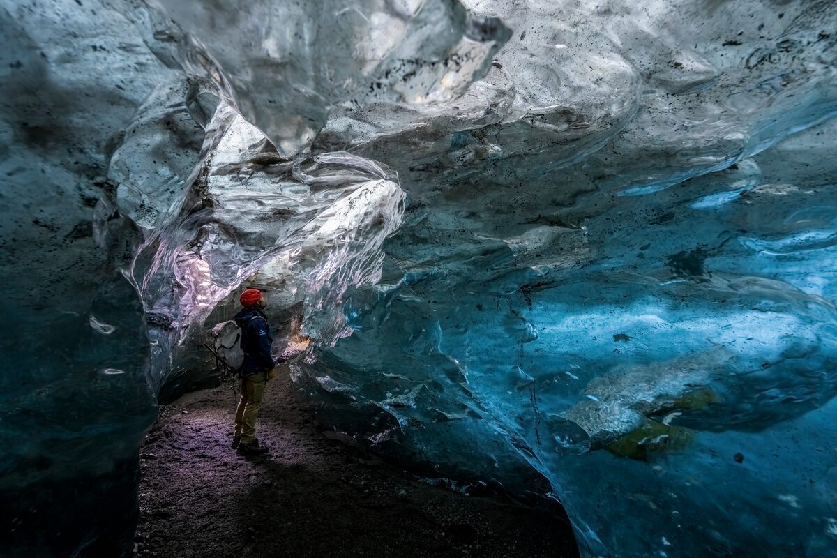 Tourist inside blue crystal ice cave by Vatnajokull, looking at crystal blue ice cave walls.