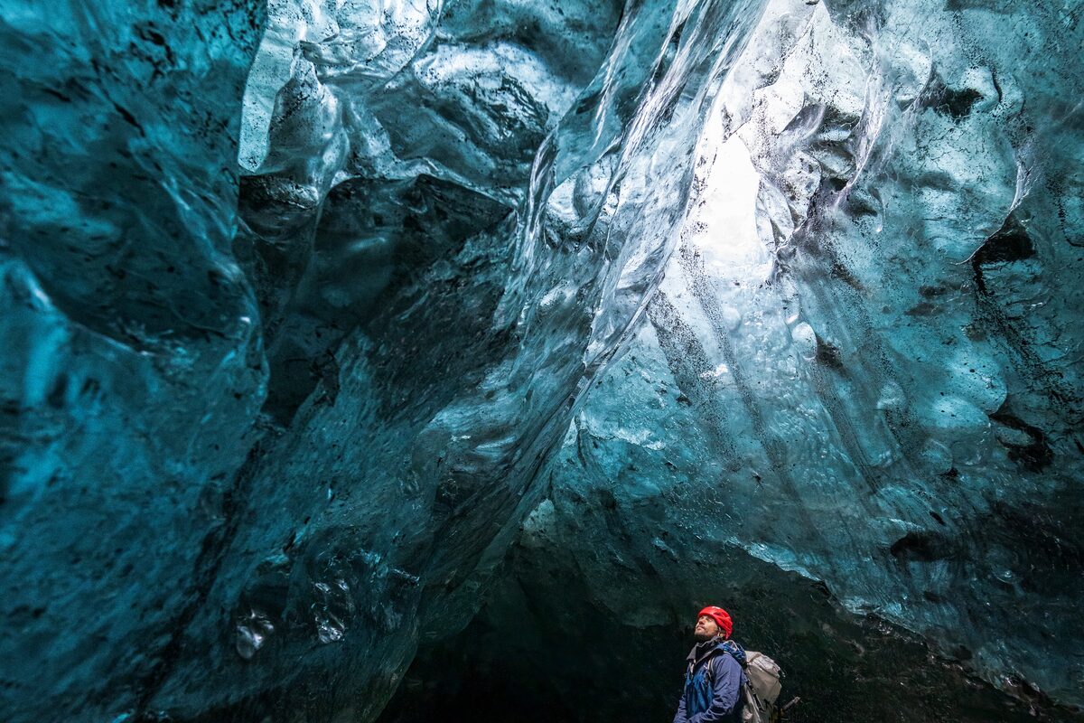 Tourist looking up to light reflecting off blue crystal ice cave walls in Iceland, 2025.