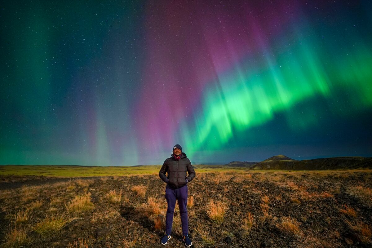 Male tourist posing underneath northern lights during autumn at lava fields in south west Iceland.