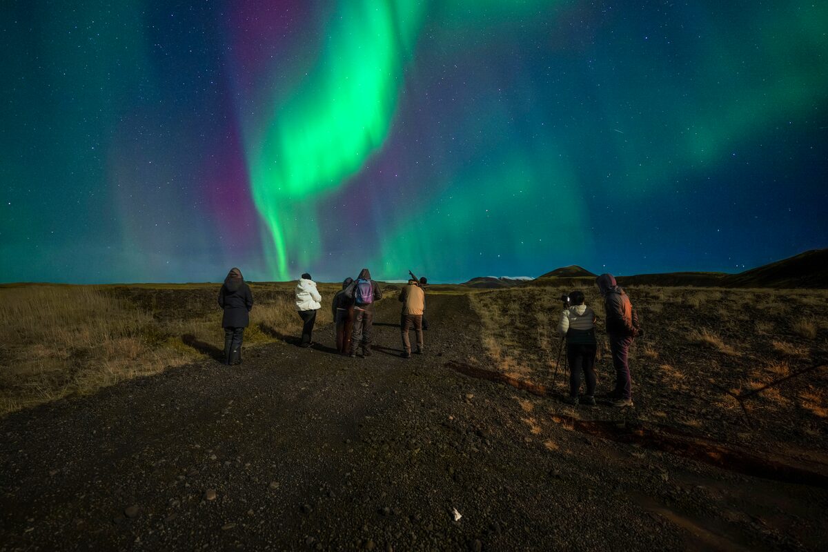Small group of tourists walking along a road in Iceland during night looking up at the Aurora Borealis.