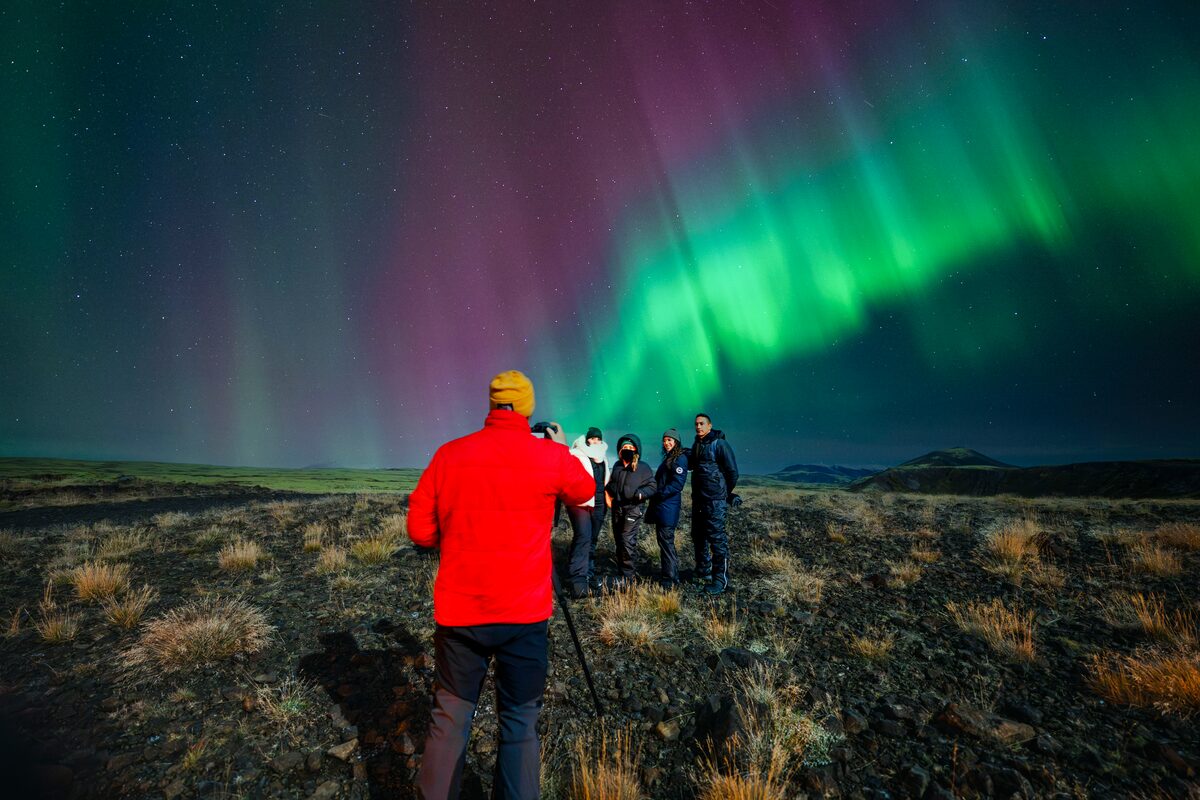 Arctic Adventures tour guide taking a photograph for a group of tourists standing underneath the Aurora Borealis.