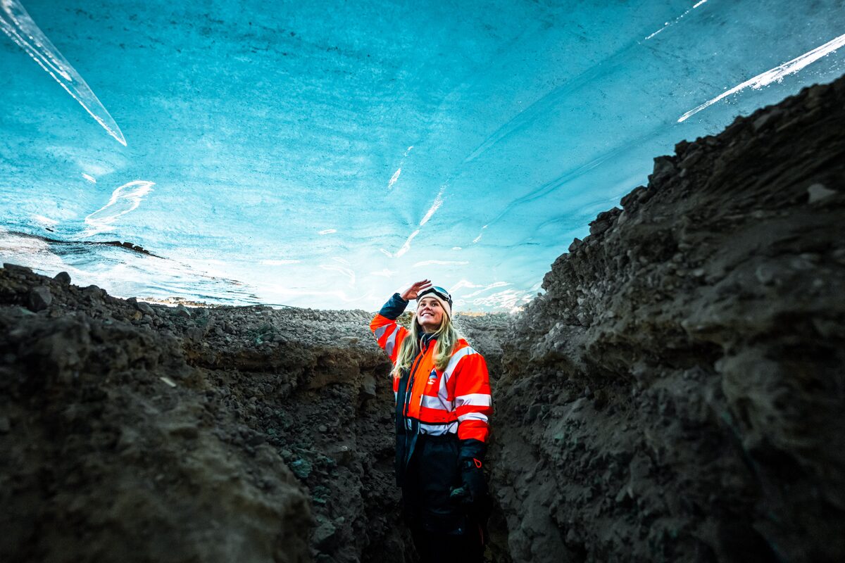 Female posing for photo inside bright blue ice cave at Langjokull glacier in Iceland.