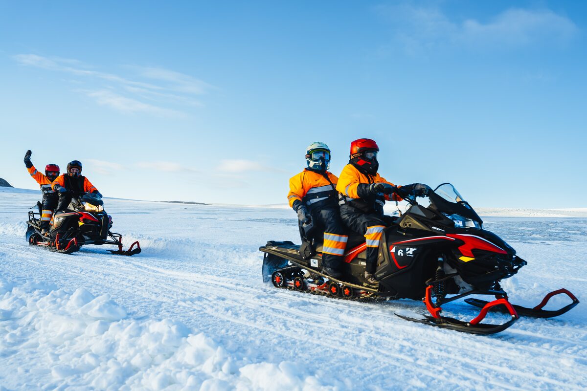 Group of four tourists snowmobile riding across Langjokull glacier in Iceland.