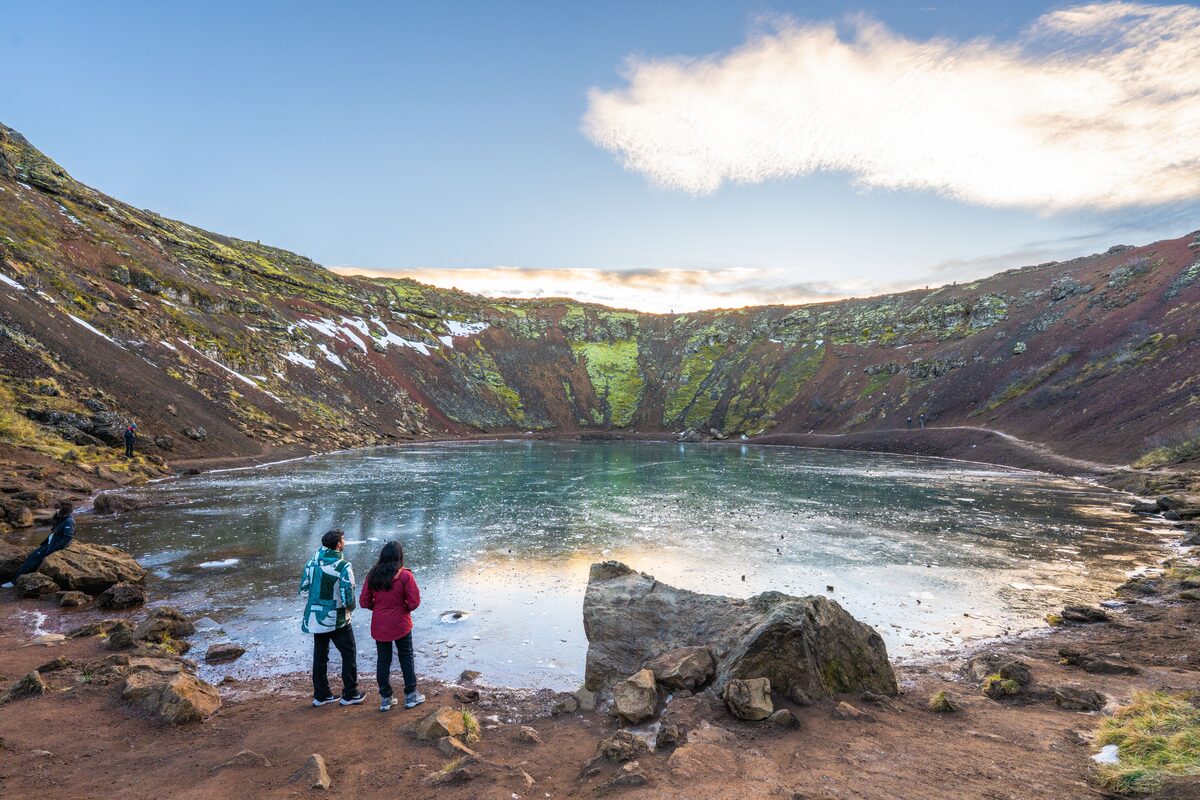 Couple standing inside Kerid Volcanic crater, next to lake and huge rock in winter.