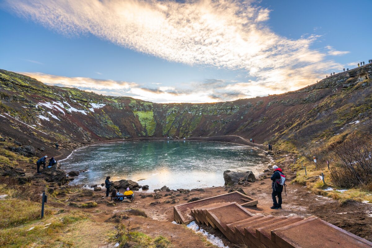 Tourists photographing Kerid Volcanic crater lake from footpath steps leading down to lake.