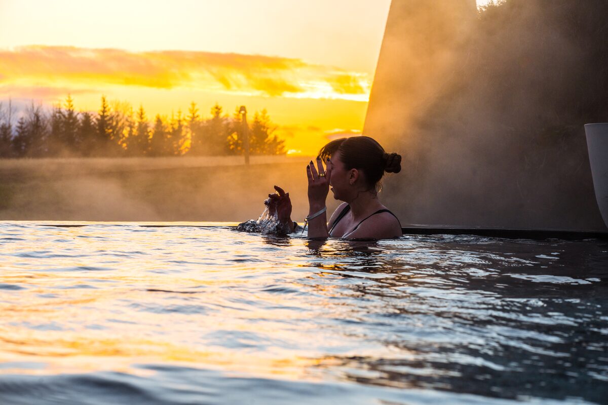 Woman bathing in Krauma geothermal baths in Iceland during golden sunset.