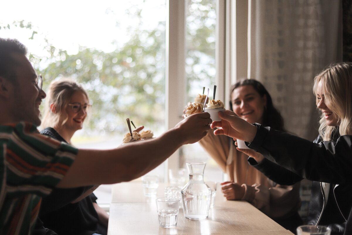 Four friends holding up their ice cream desserts to cheers, in a restaurant in Reykjavik.
