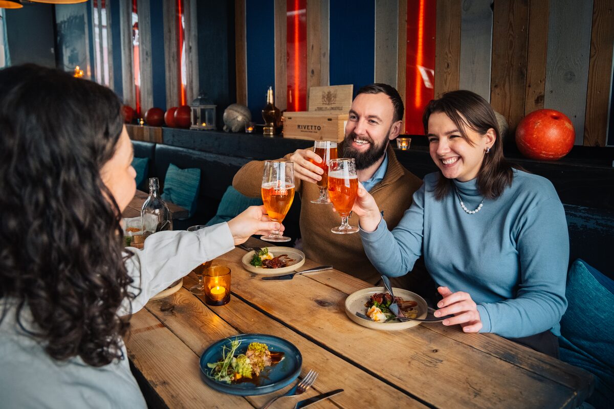 Group of three friends making cheers with beers in an Icelandic bar in Reykjavik city.