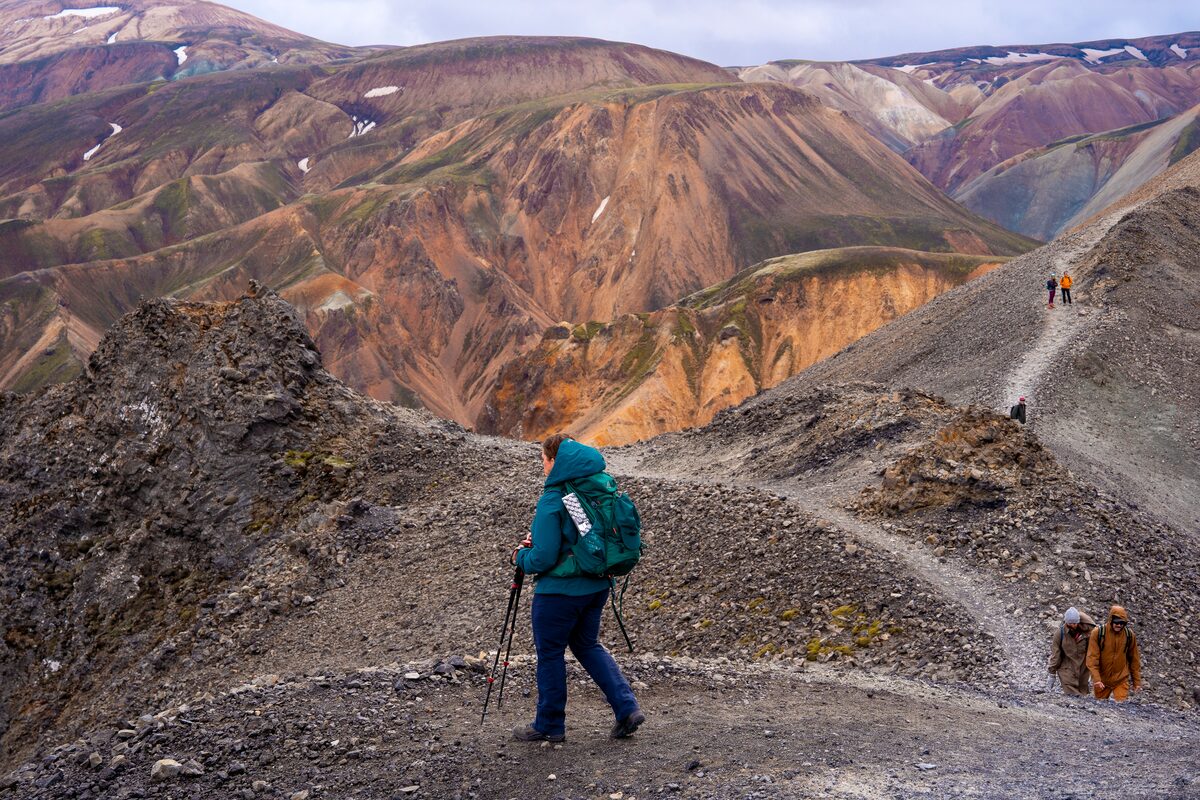 Women with hiking sticks hiking across mountain terrain and lava fields in the Laugavegur trail.