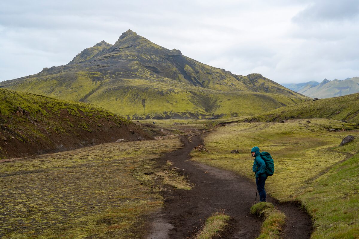 Male hiker walking towards a moss covered mountain on Laugavegur trail in Iceland in summer.