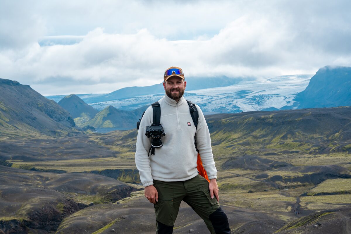 Man posing for photo on the Laugavegur hiking trail, standing in front of glacier in distance.