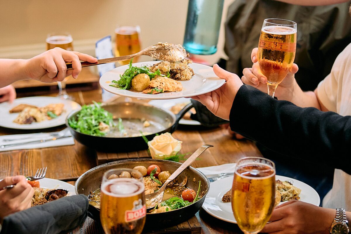 Close up of table in restaurant filled with hot meals and friends creating a cheers with Icelandic beer.