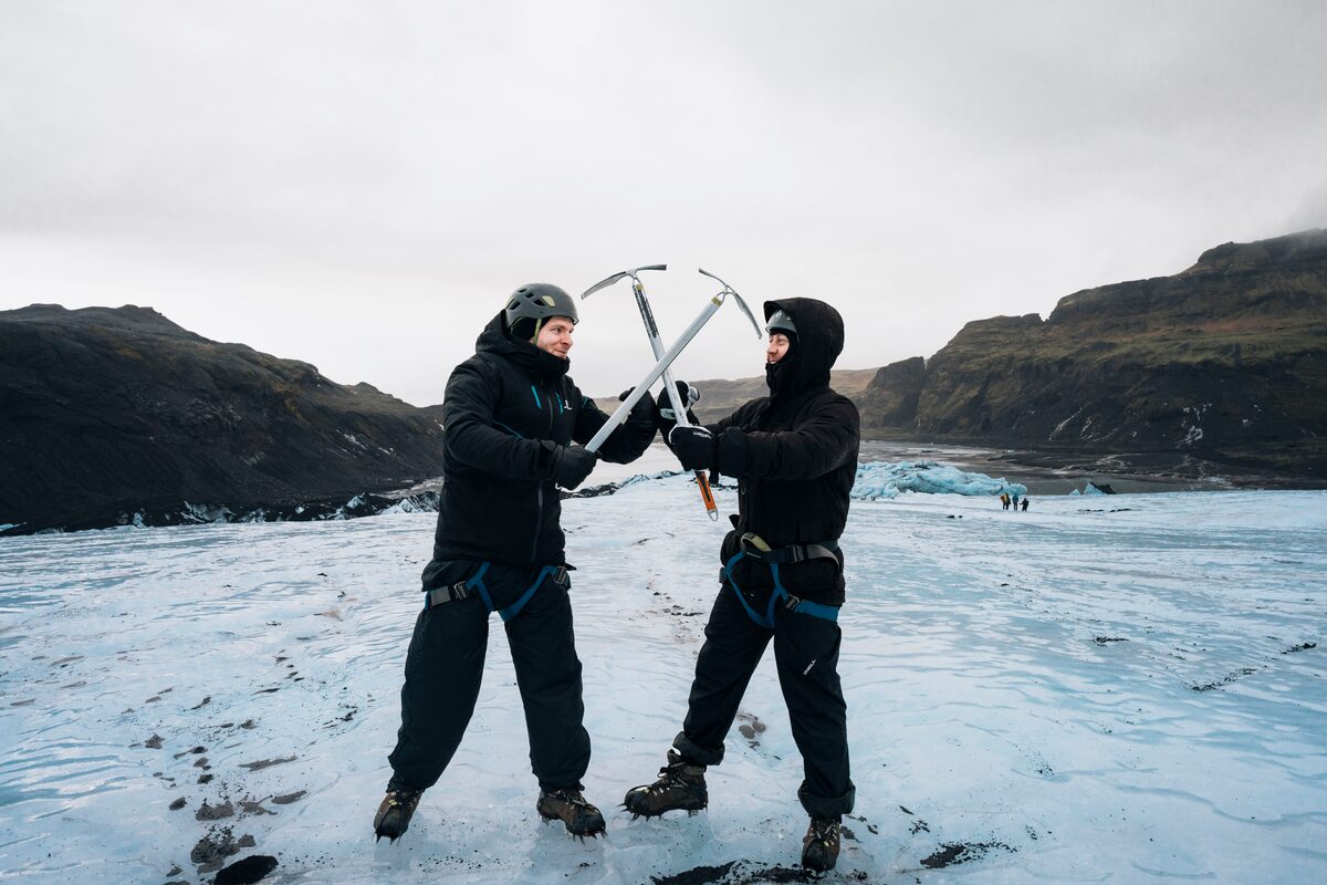 Two male tourists posing with two ice pick axes on Solheimajokull glacier in Iceland.