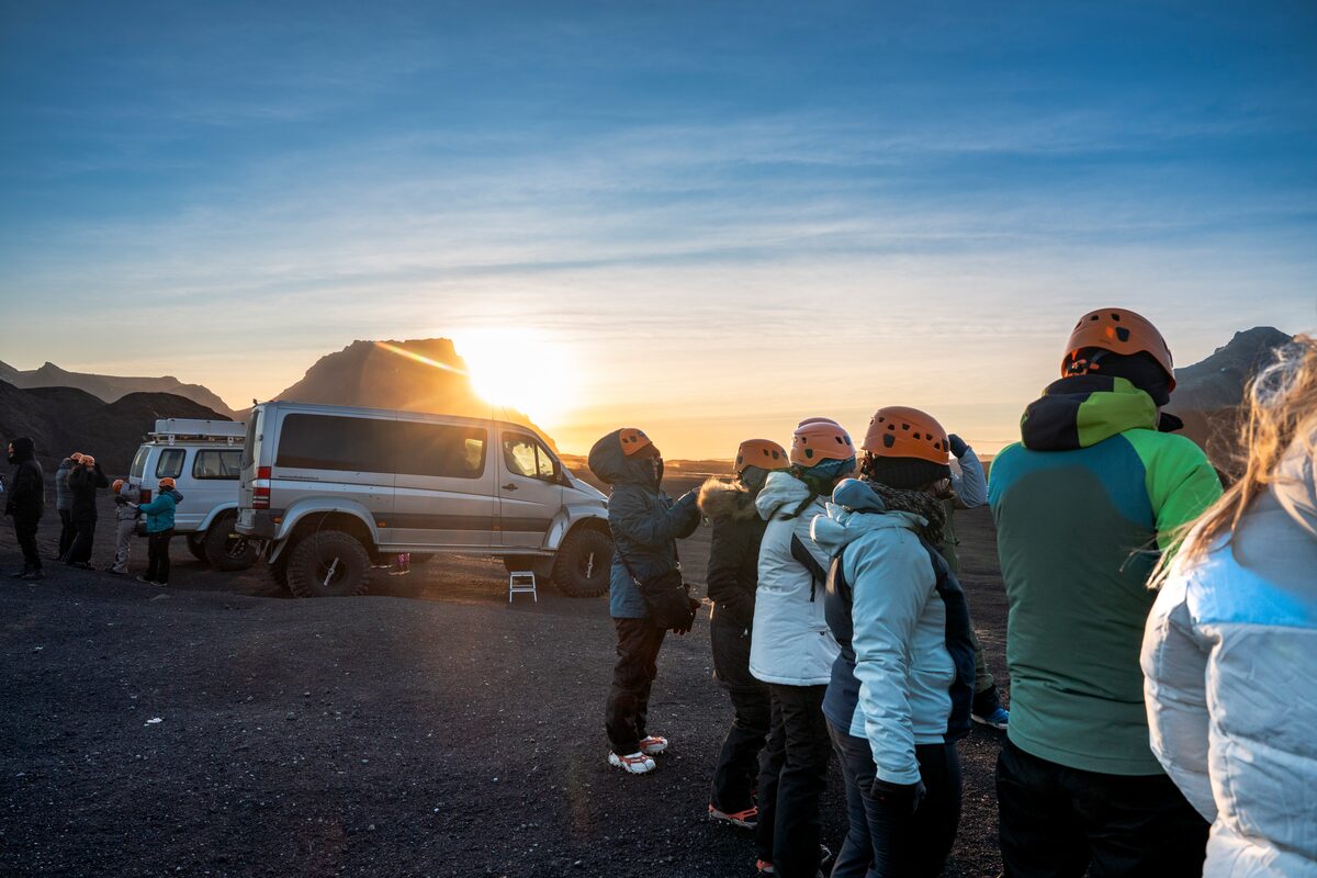 Small group of tourists standing at Katla parking area next to silver super jeep, during sunset.