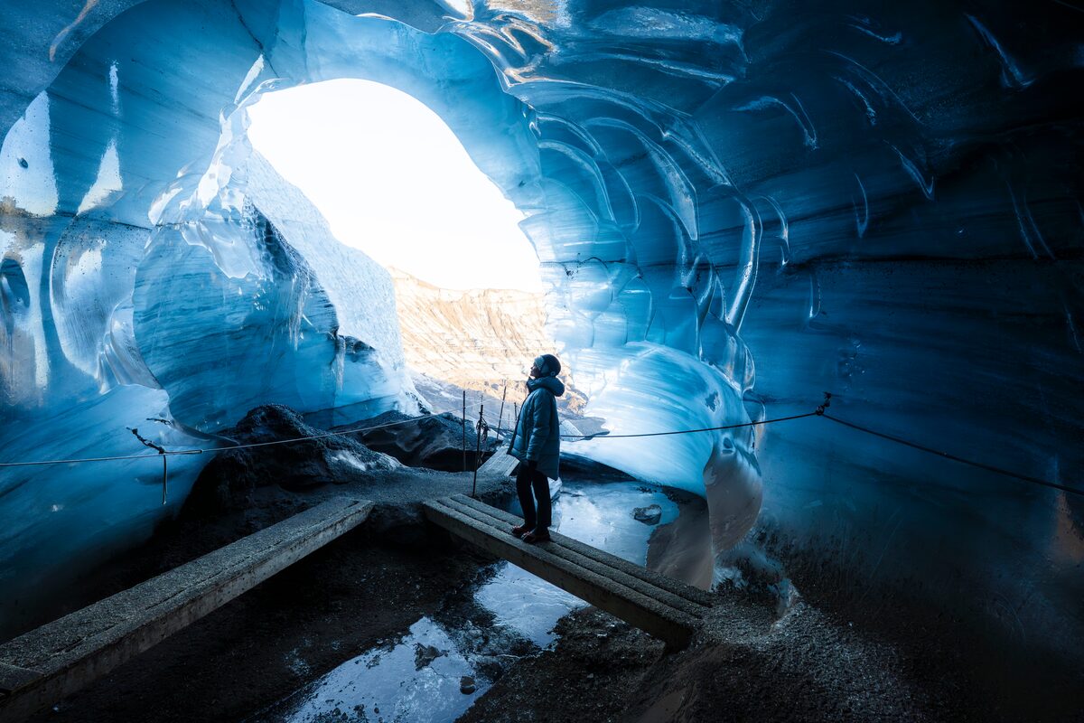 Female tourist posing for photo next to blue Katla walls, on wooden bridge inside the ice cave.
