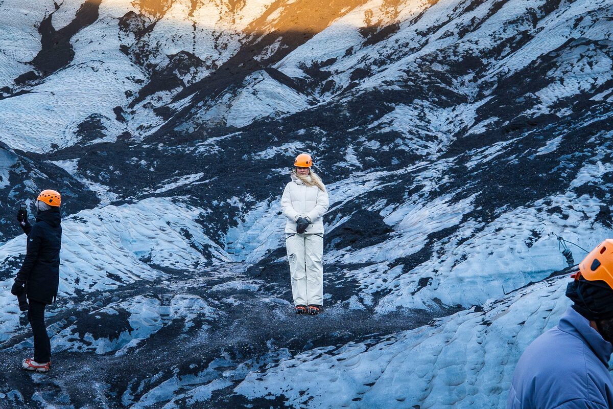 Female tourist standing on Kotujokull outlet glacier in Iceland amongst patterned white and black glacier ice.