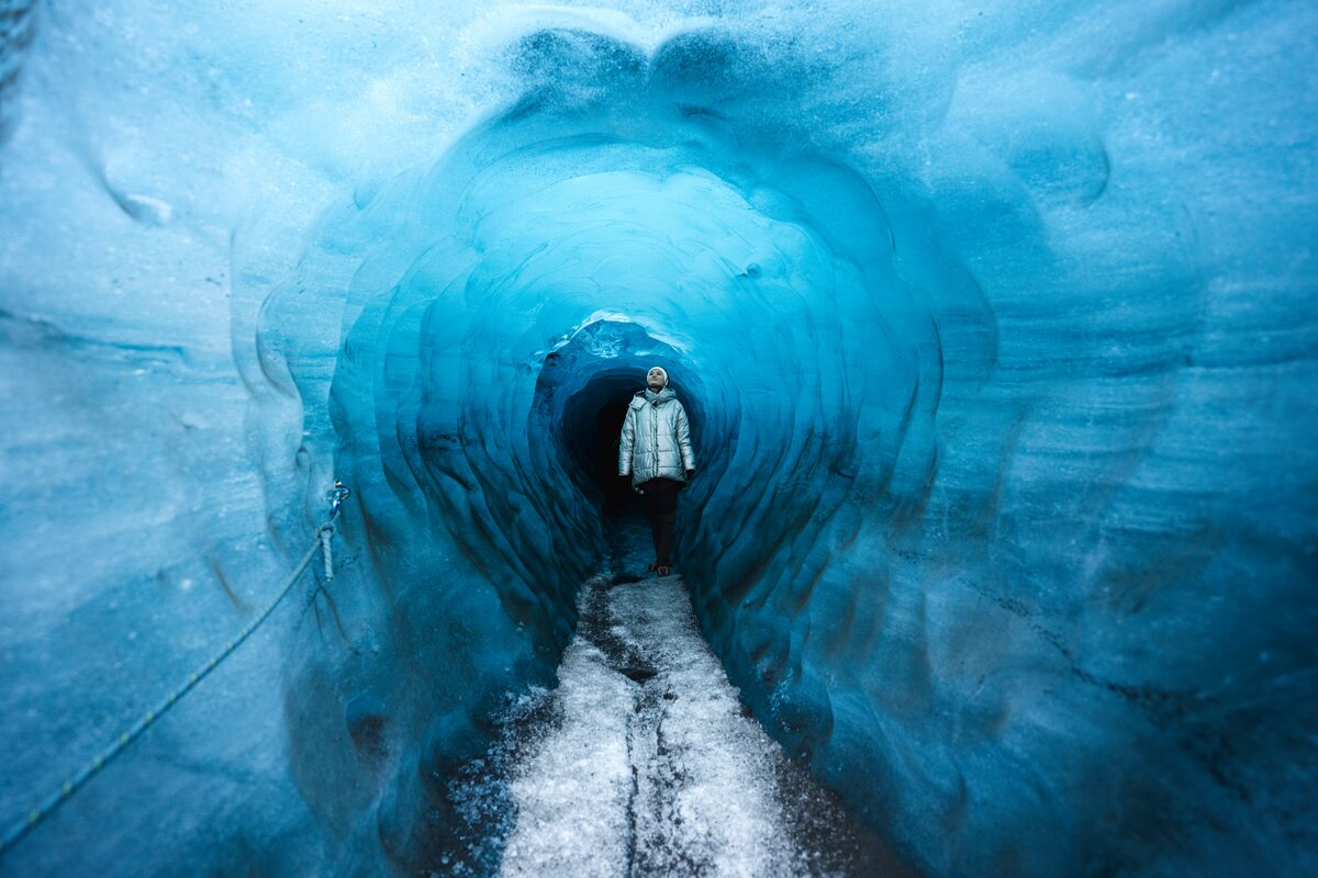 Tourist walking through Katla ice cave, bright blue ice cave walls reflecting the light.