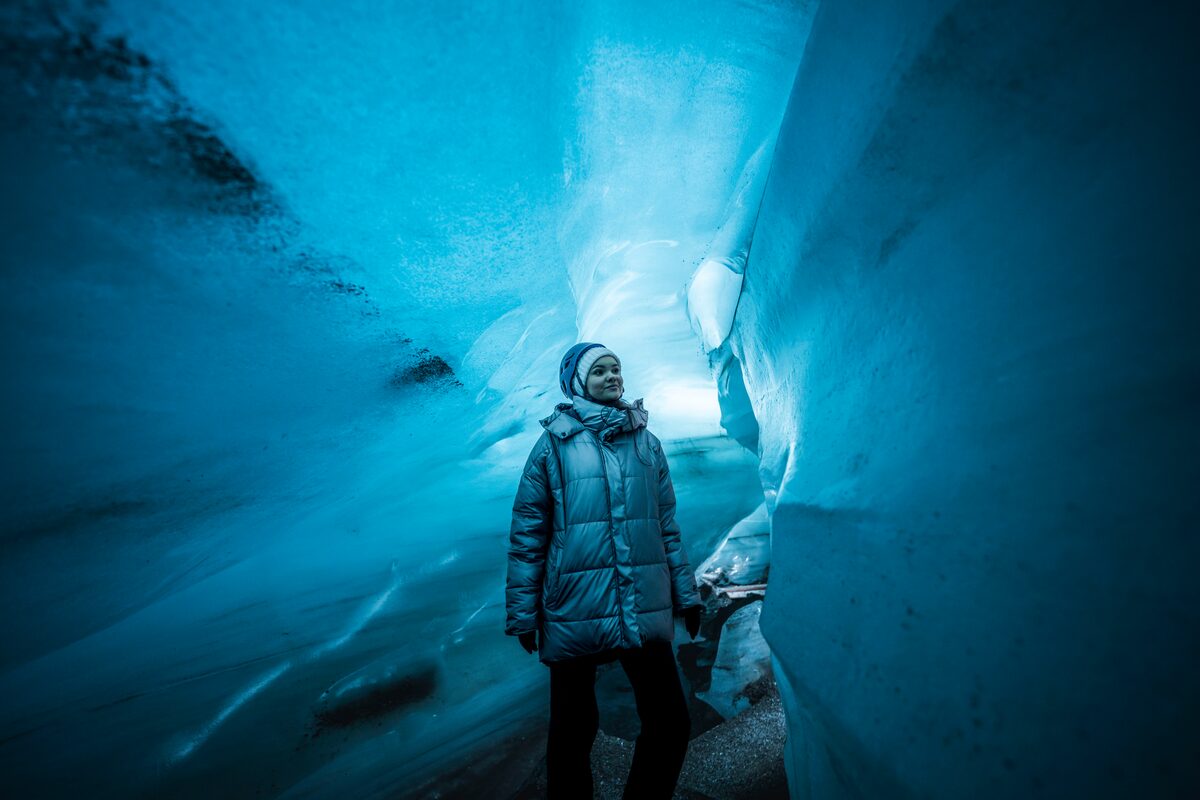 Close up of tourist standing inside Katla ice cave against bright blue ice walls.