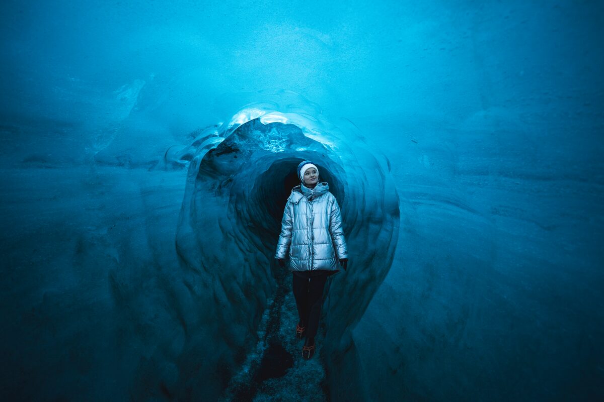 Female tourist walking through blue Katla ice cave in Iceland during winter.