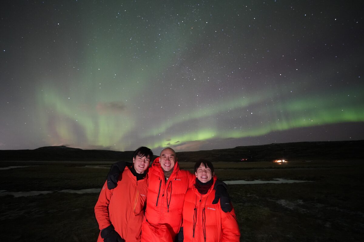 Three Men In Red Jackets Posing Under Northern Lights in iceland