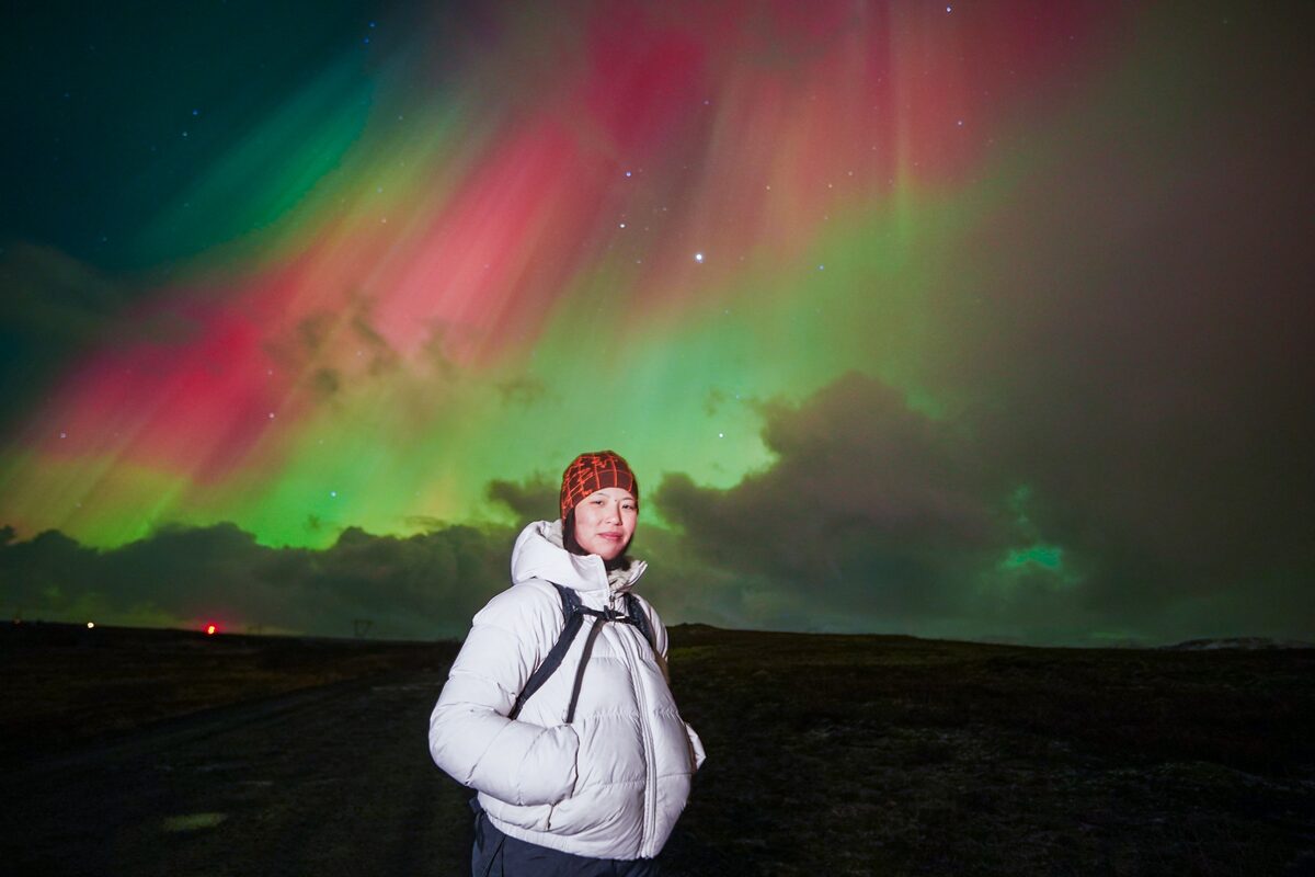Female tourist posing for magical auroras in night sky in Iceland