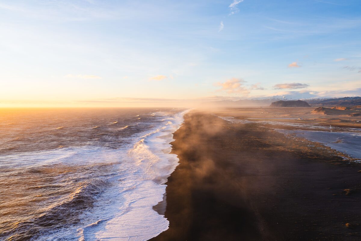 Aerial view of Iceland’s South Coast with waves breaking along a long black-sand beach in golden evening light