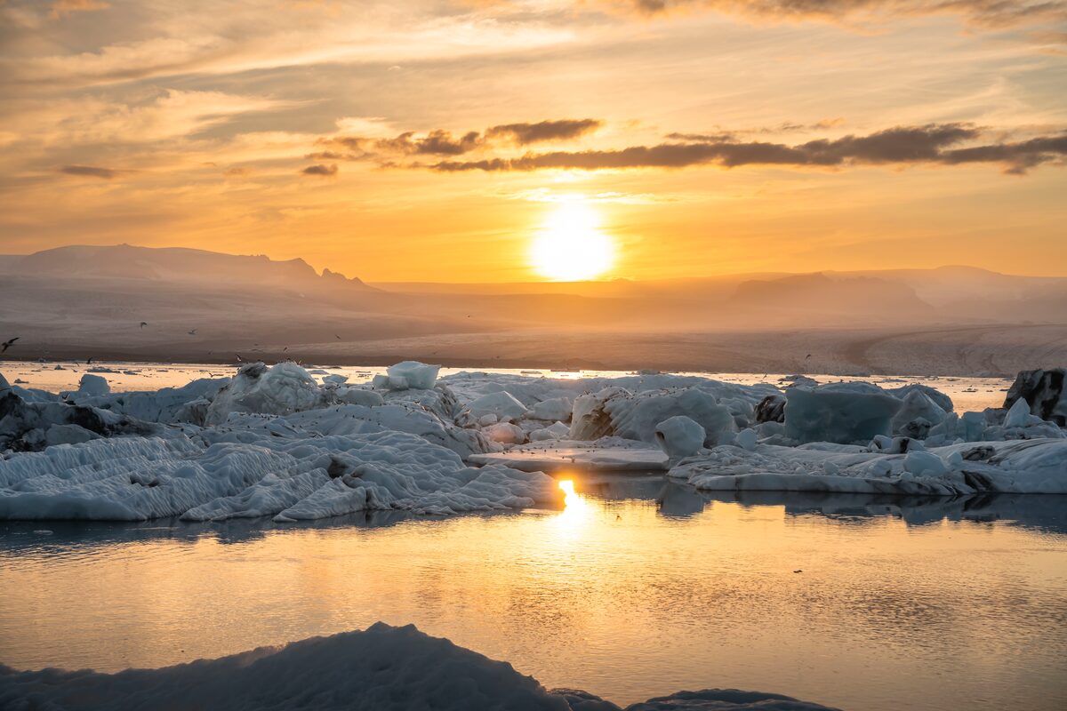 Golden summer sunset reflecting on calm water with floating icebergs at Jökulsárlón Glacier Lagoon, South Coast Iceland
