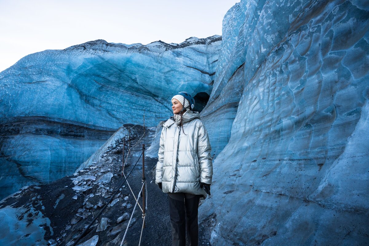 Tourist in a silver parka stands beside blue glacier ice inside Katla Ice Cave, Iceland