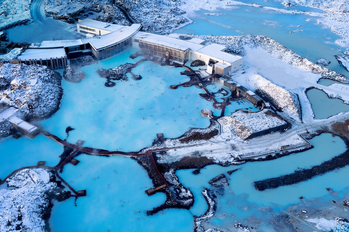 Blue Lagoon at night with steam rising over milky-blue water, lava rocks, and people bathing.