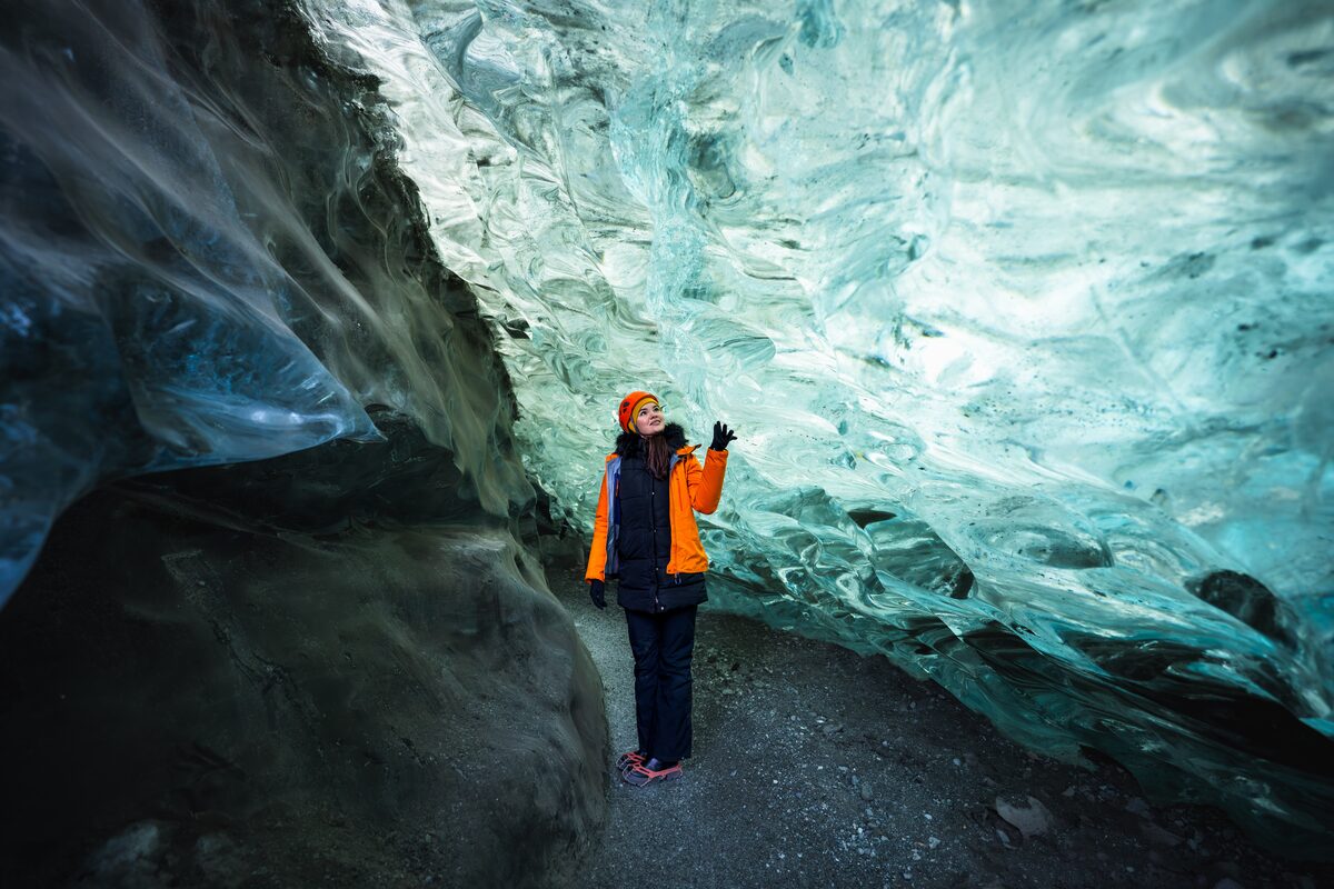 Female tourist standing inside crystal ice cave in Iceland, reaching for ice cave wall.