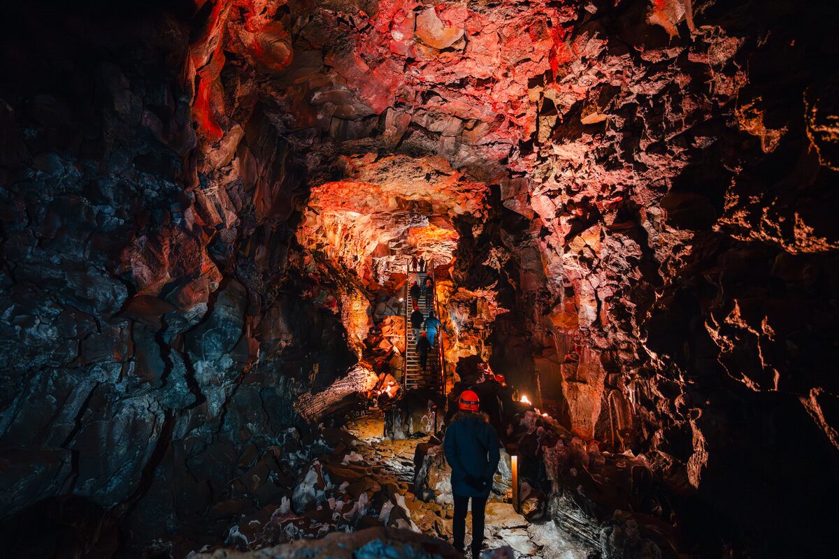 Interior of Raufarhólshellir lava tunnel with a staircase leading up and lines of people walking.