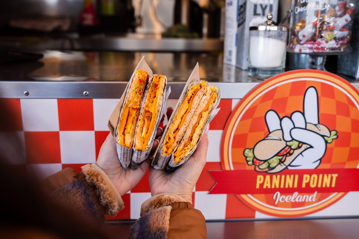 Two grilled panini sandwiches held up in front of a red Panini Point food truck counter.