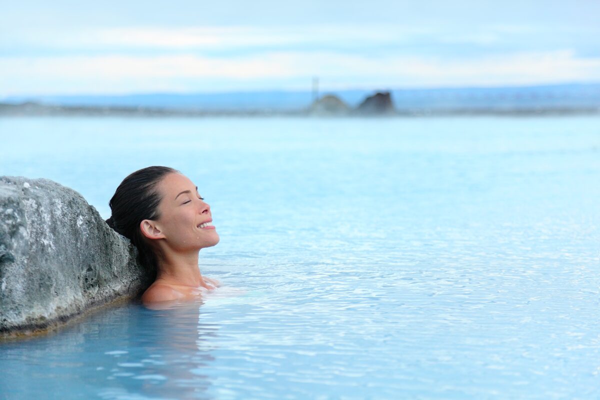 Person relaxing in milky-blue geothermal water with hair tied back. 