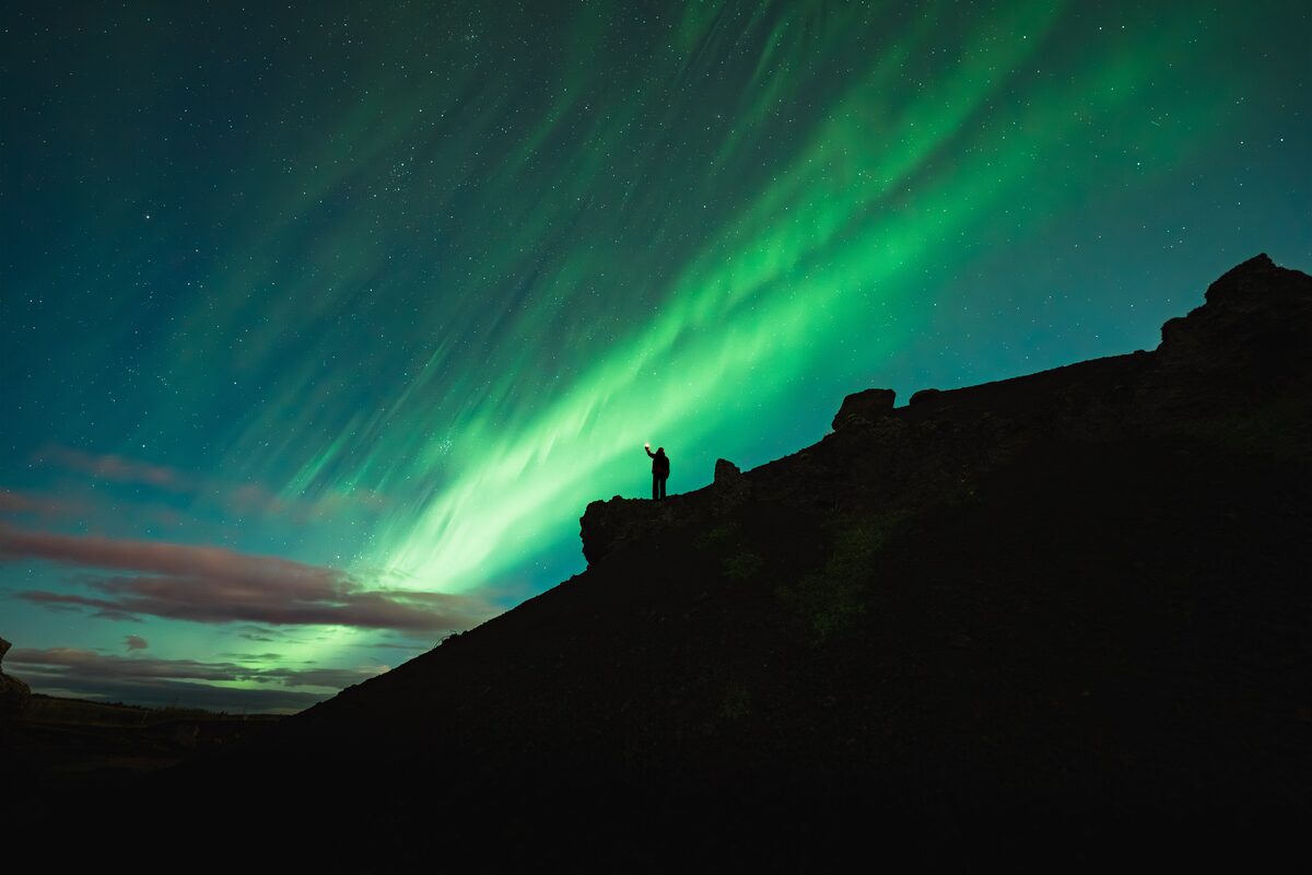 Silhouette of a person under an aurora with a wide landscape framing.